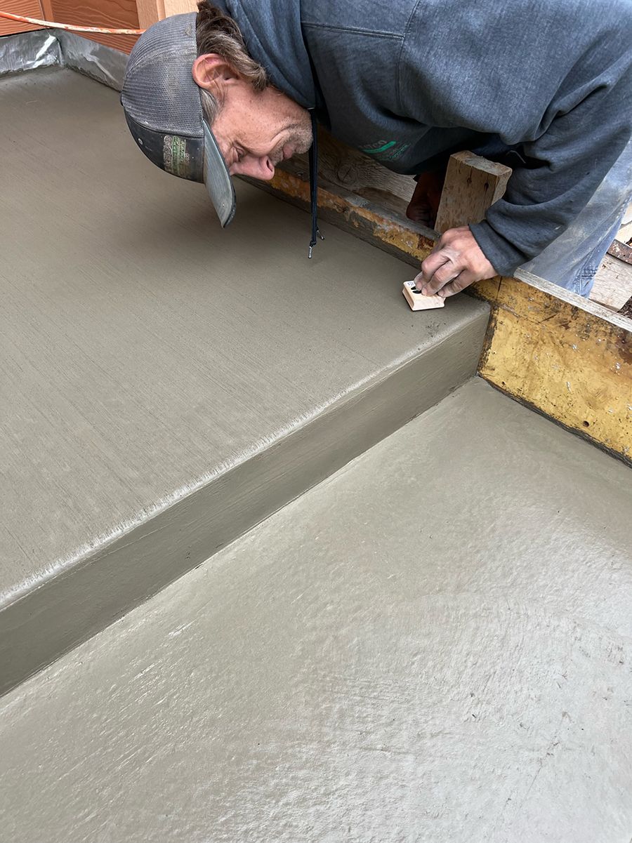 Man smoothing wet concrete with a sponge. Wearing a hat and gray sweatshirt.