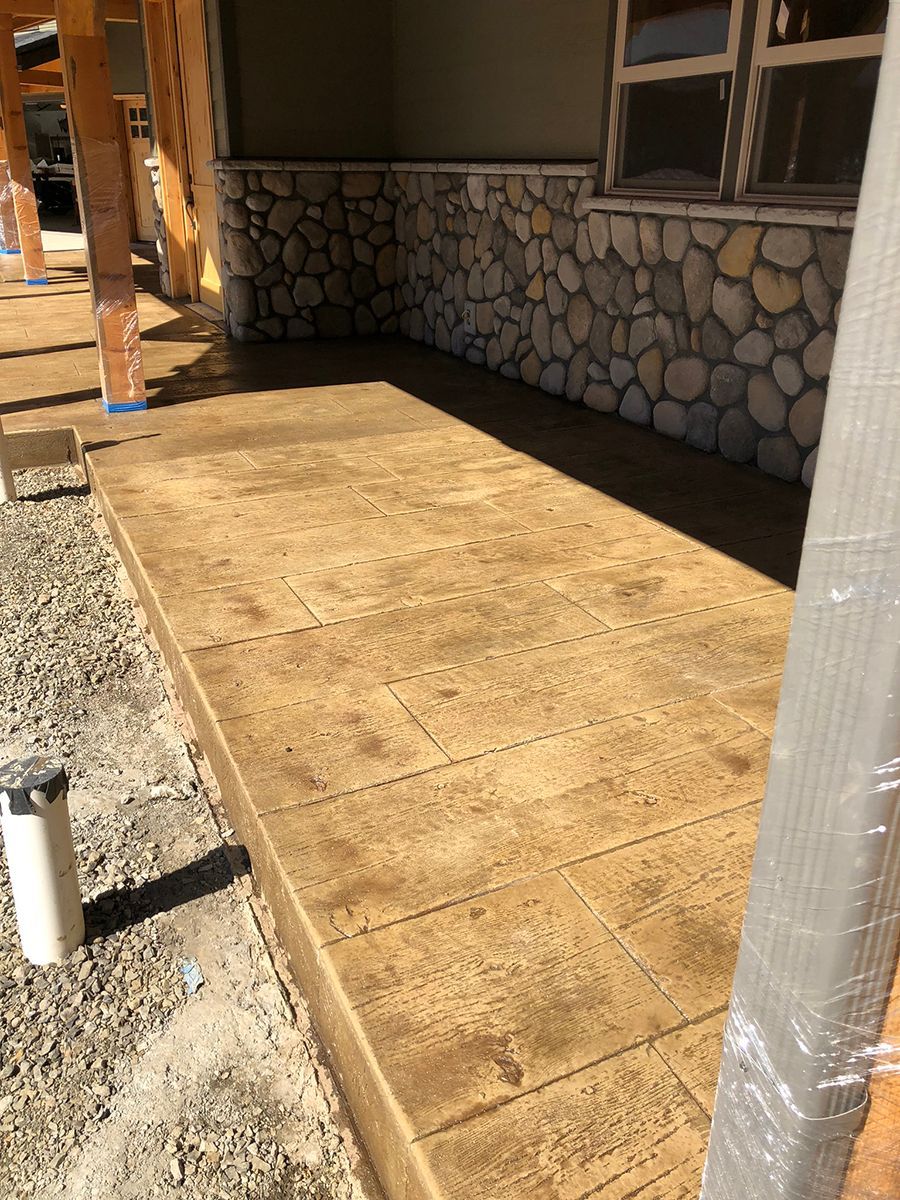 Brown stamped concrete patio with stone wall and window.