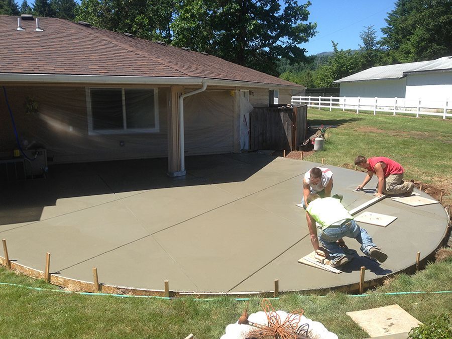 Workers pouring and smoothing concrete for a patio next to a house with a green lawn.