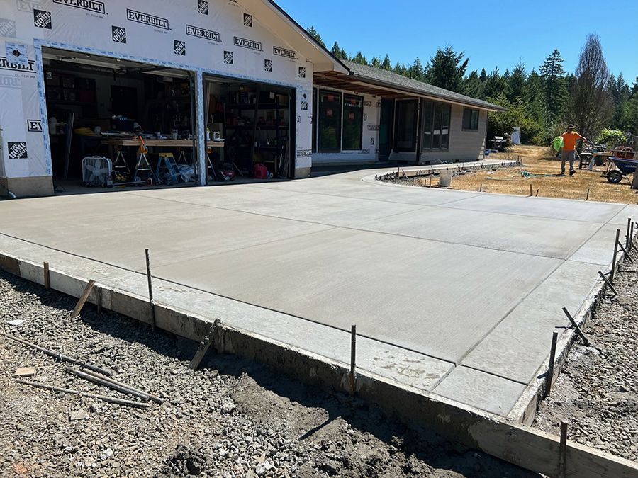 Freshly poured concrete driveway in front of a house under construction; a worker in the background.