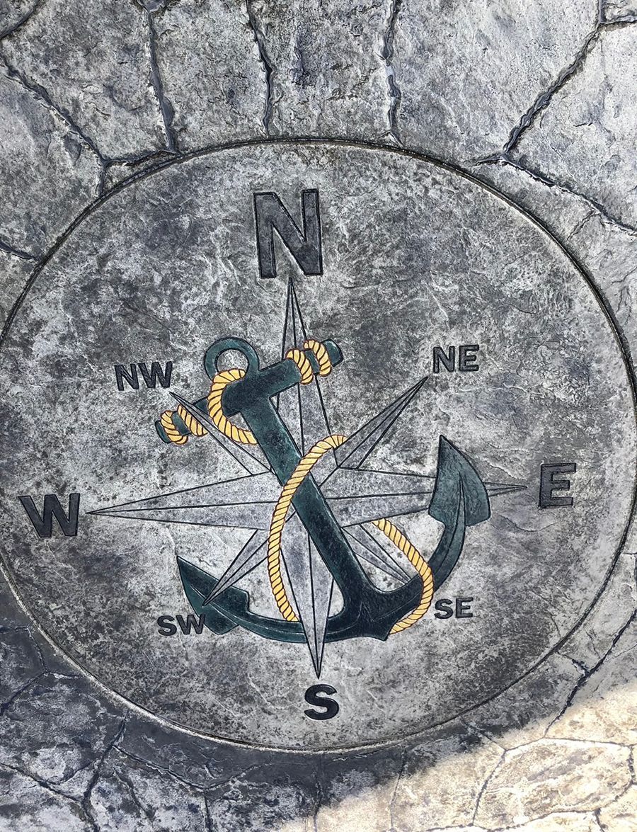Compass rose with anchor design, etched in gray stone. Directions are labeled: N, S, E, W, NE, NW, SE, SW.