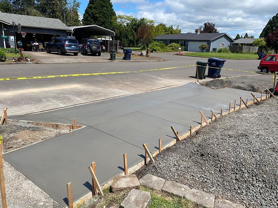Newly poured concrete driveway with wooden forms, bordering a gravel and grass yard, in a residential area.