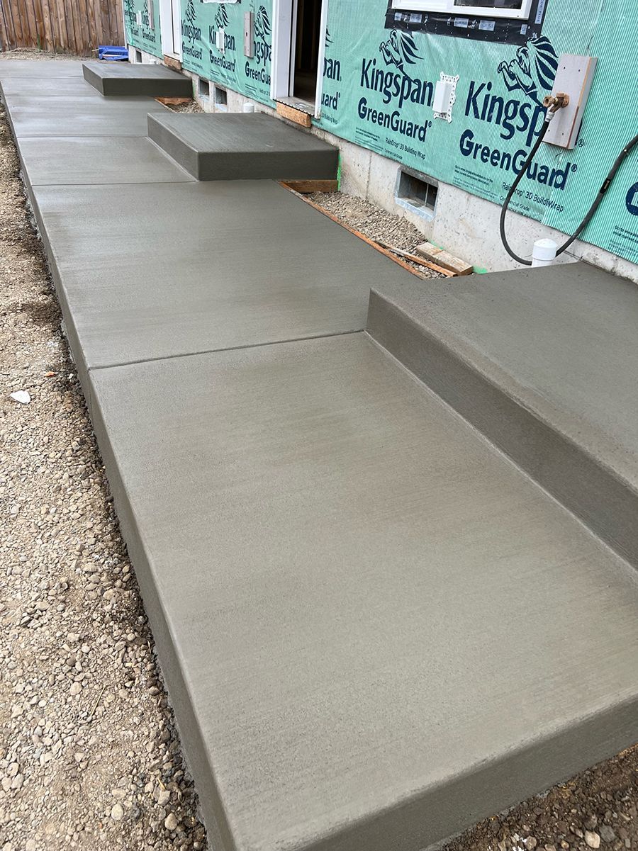 Freshly poured concrete sidewalk and steps leading to a building under construction.