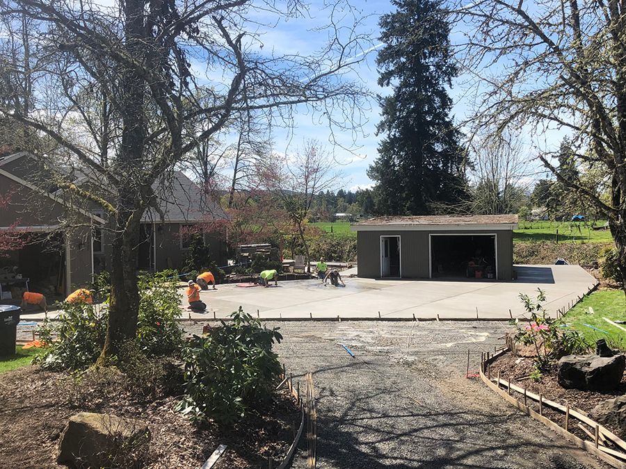 Workers pouring concrete for a driveway near a garage and house on a sunny day.