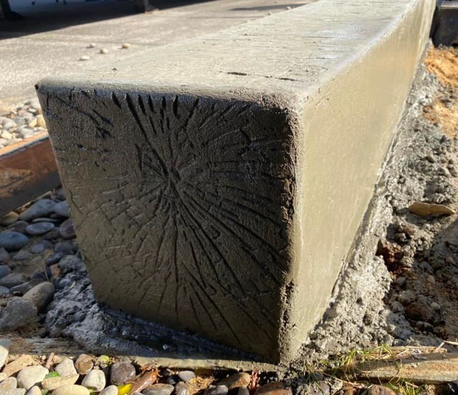 Concrete bench with textured end, set on gravel, outdoors.