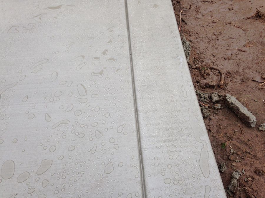Close-up of a concrete sidewalk with water droplets, next to dirt and a small concrete edge.