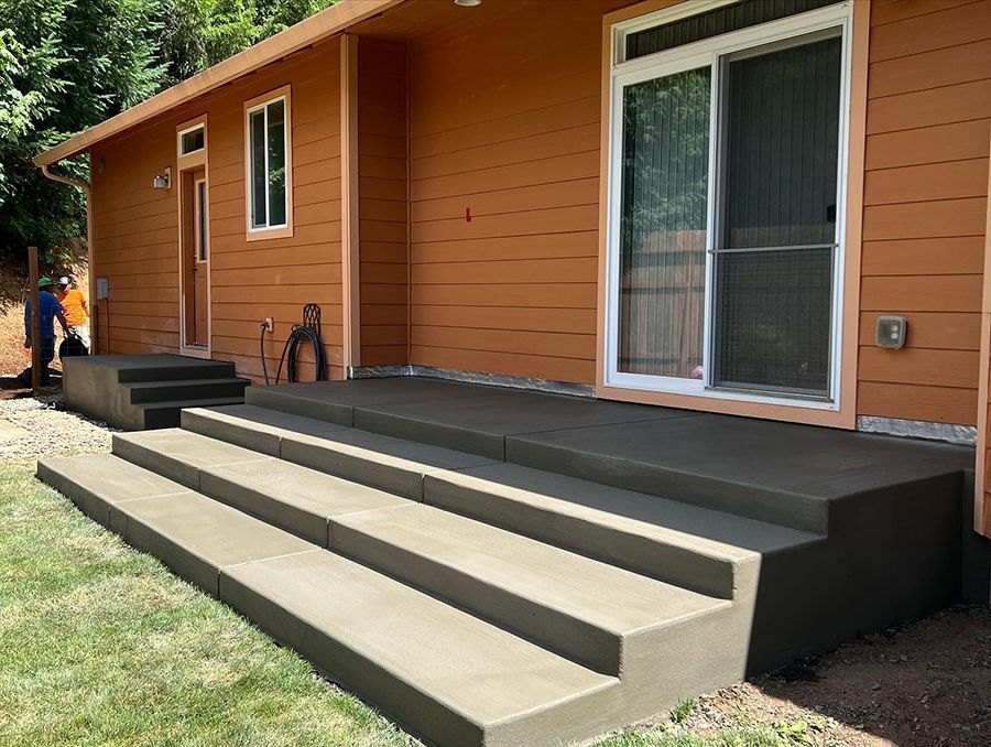 Newly poured concrete steps and landing outside an orange house with a sliding glass door.