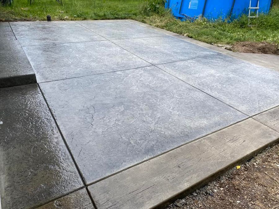 Newly poured concrete patio, divided into sections, wet, with a retaining border.