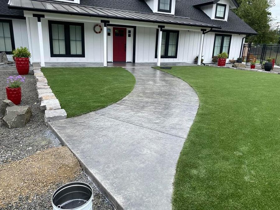 White house with a gray curved concrete path, green lawn, red front door, and black trim.