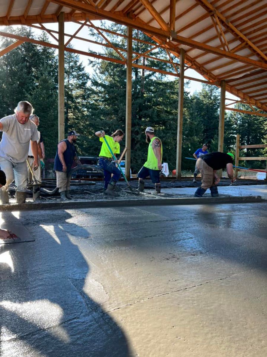 Construction workers pouring and smoothing concrete inside a wooden-framed barn.