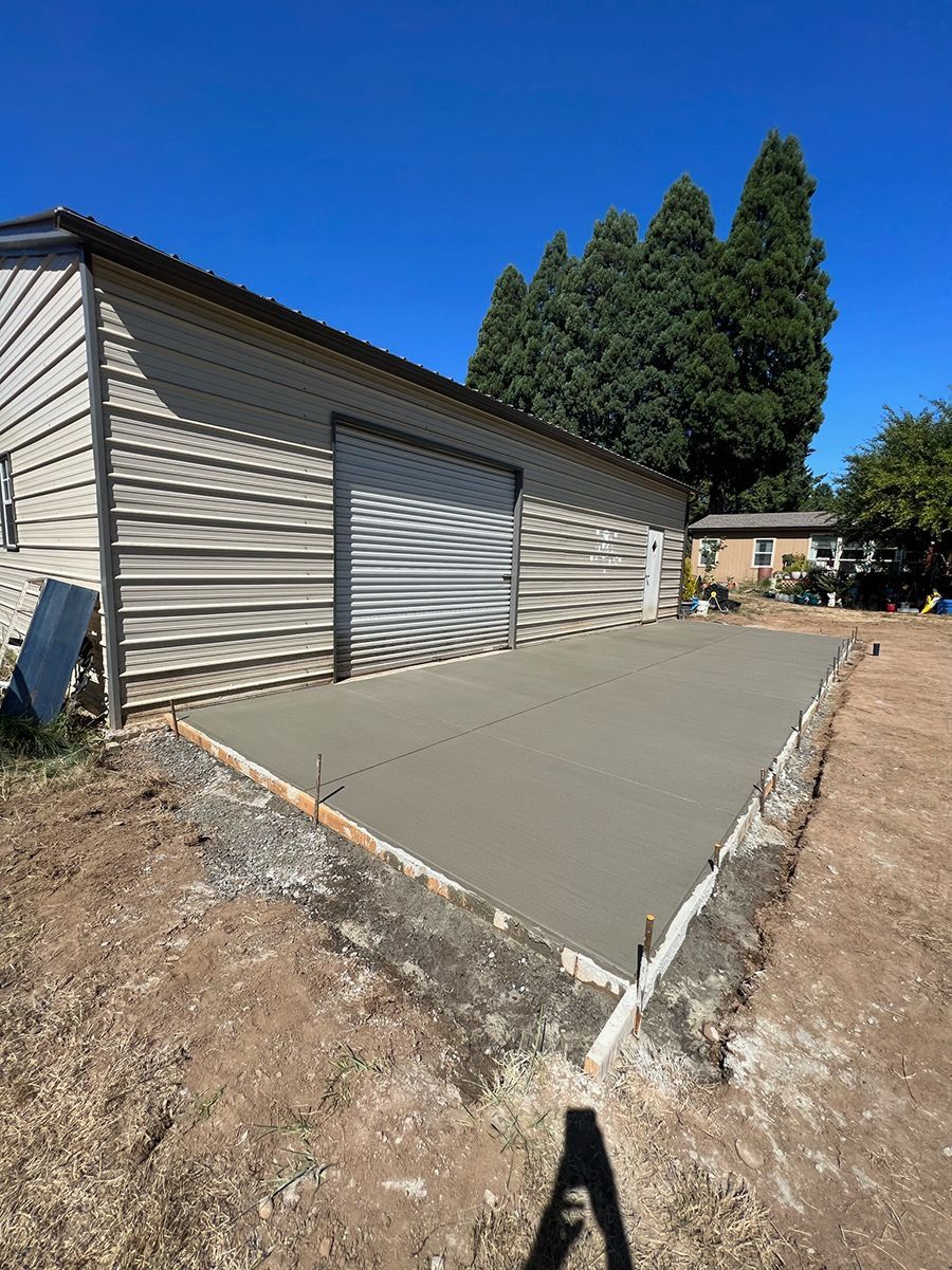 New concrete slab next to a metal building with a garage door, on a sunny day.