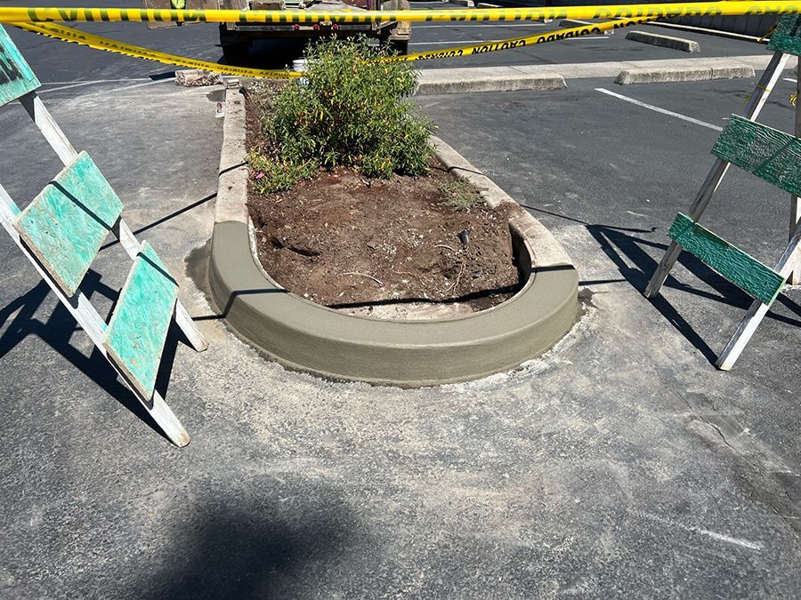 Newly constructed concrete planter in a parking lot, with a small bush and caution tape.