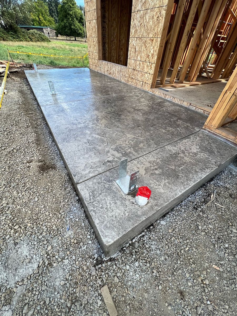 Newly poured concrete patio outside a building under construction; gravel surrounding the edges.