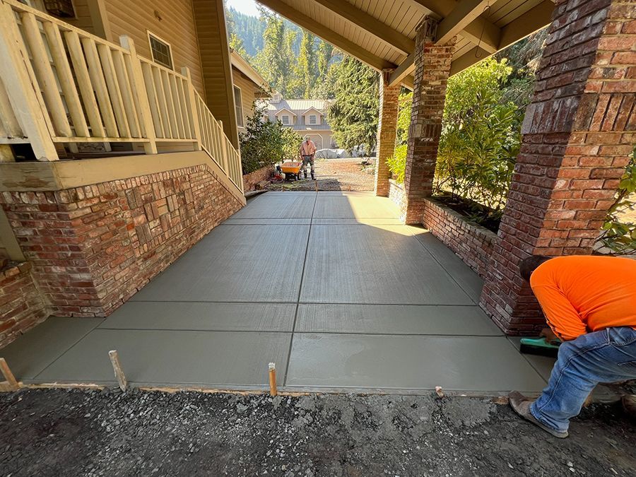 Workers finishing a new concrete driveway. Brick columns frame the covered entrance.