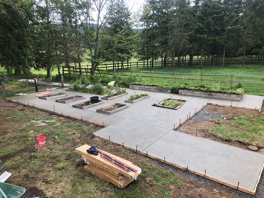 Concrete patio with raised garden beds under construction in a rural setting.