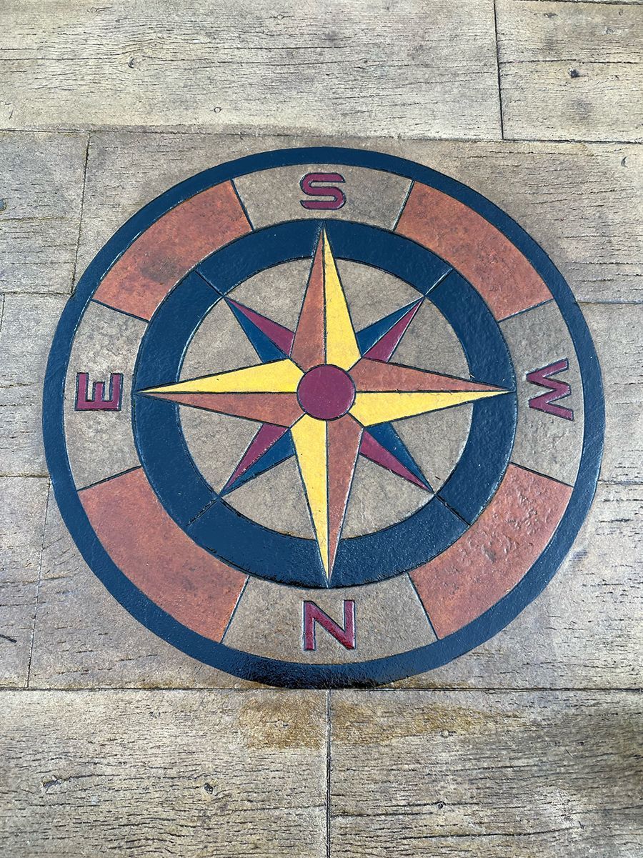 Compass rose design inlaid on a concrete surface.  Features north, south, east, and west markings in a circular pattern.