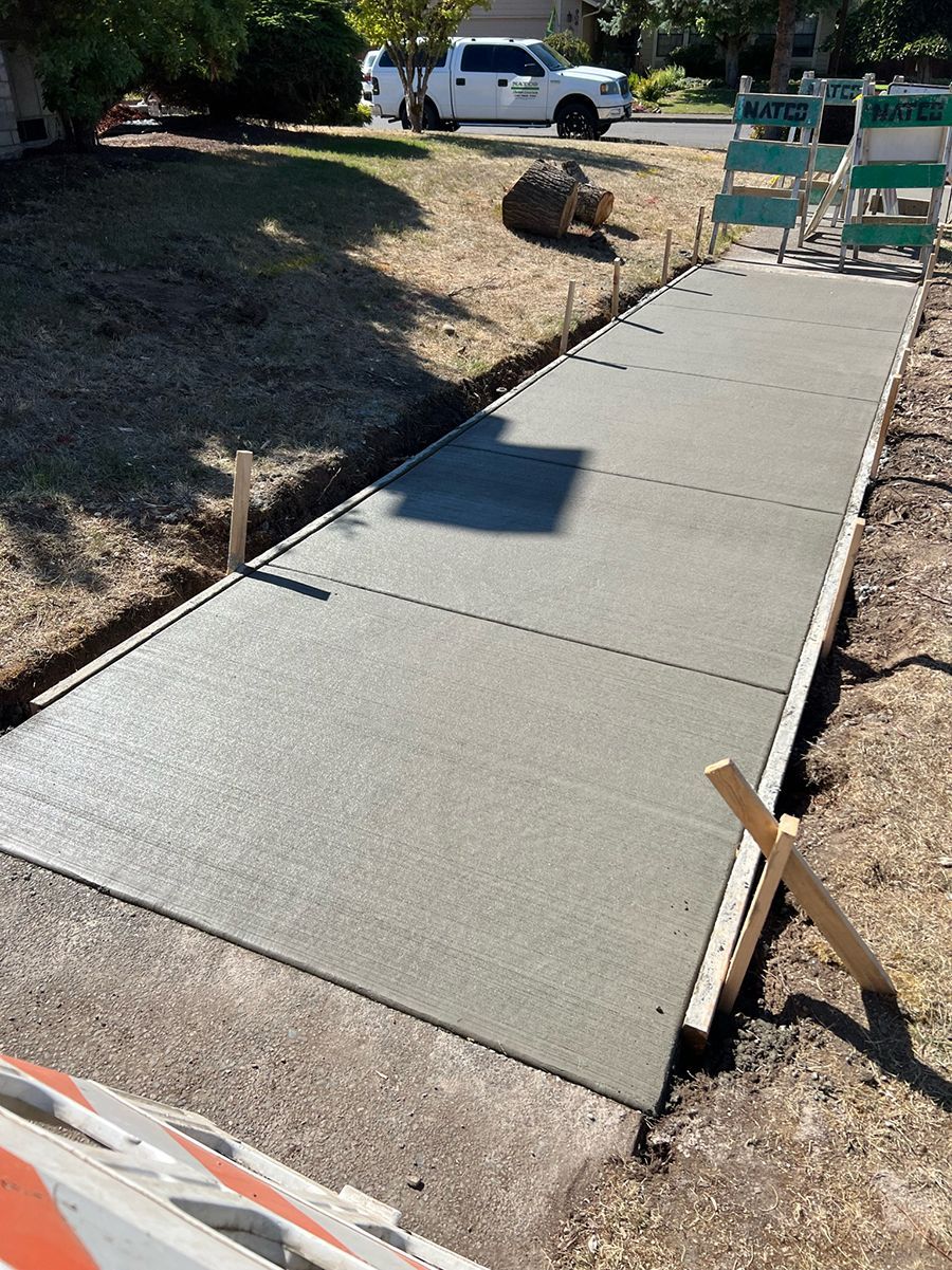 Newly poured concrete sidewalk with wooden forms in a residential yard.