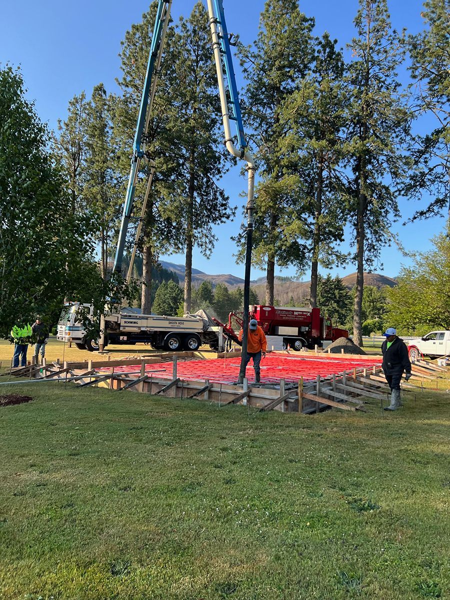 Concrete being poured for a foundation. Construction workers at the site, with trees and mountains in the background.