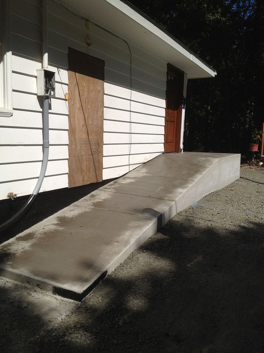Concrete ramp leading up to a building with two doors. White siding, brown doors.