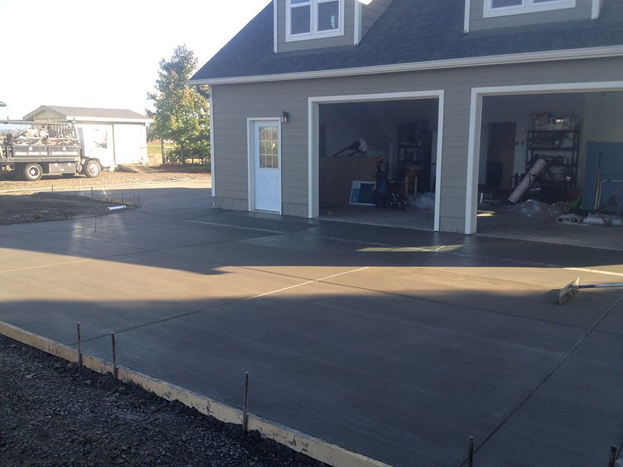 Freshly poured concrete driveway in front of a light gray two-car garage with open doors.