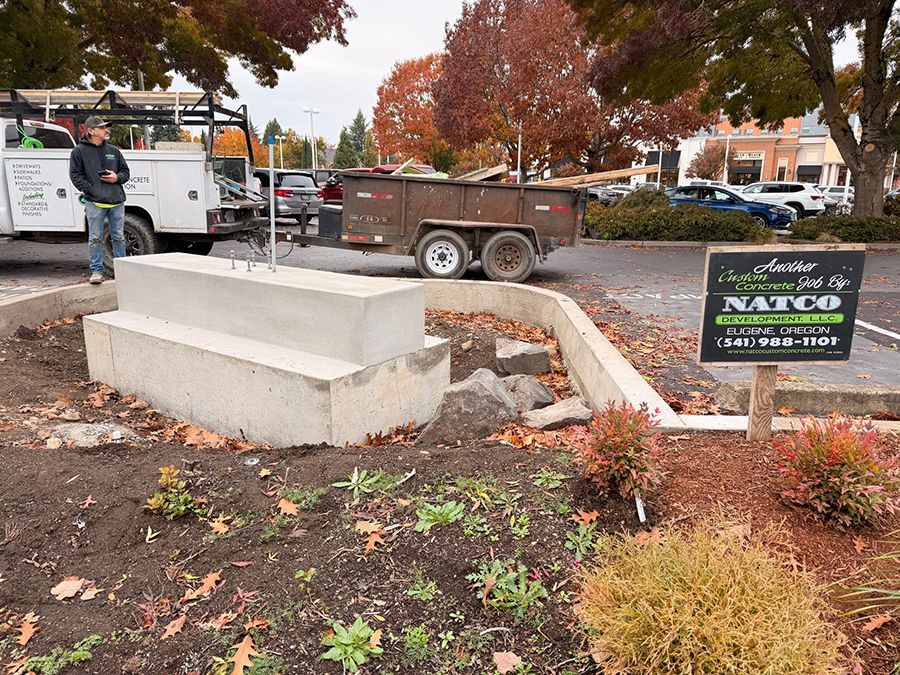 Construction site with concrete base, trailer, truck, and worker.