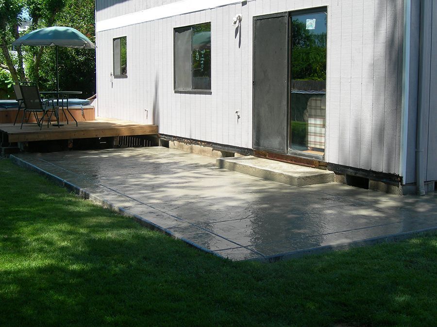 Concrete patio next to a light gray house, surrounded by green grass.