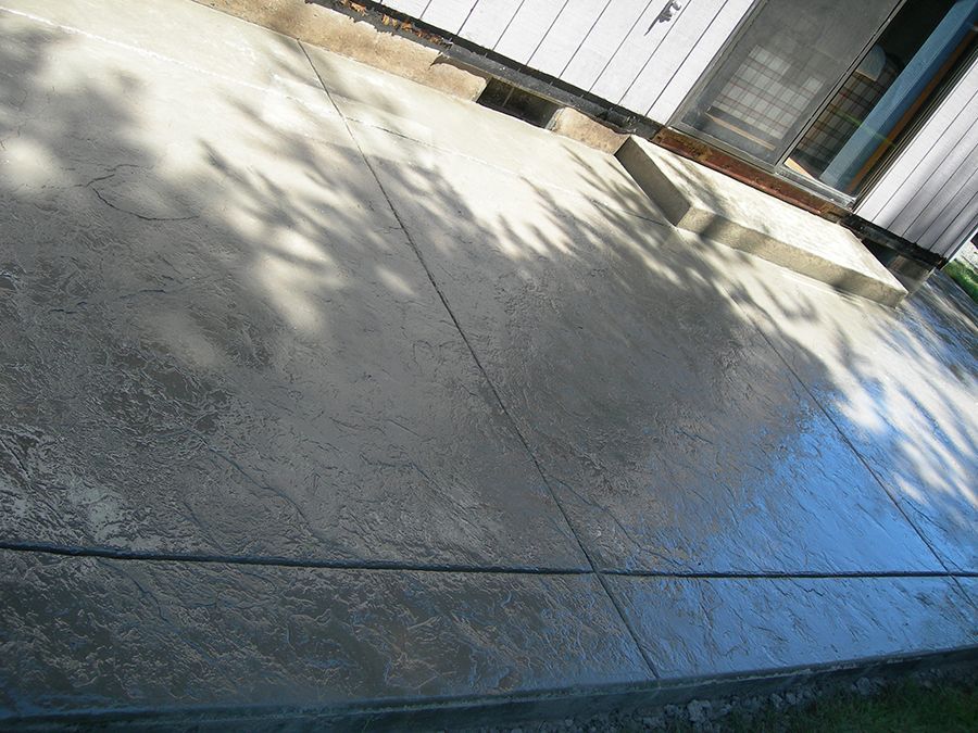 Newly poured concrete patio, sunlight casts shadows, rectangular sections, adjacent to a building.