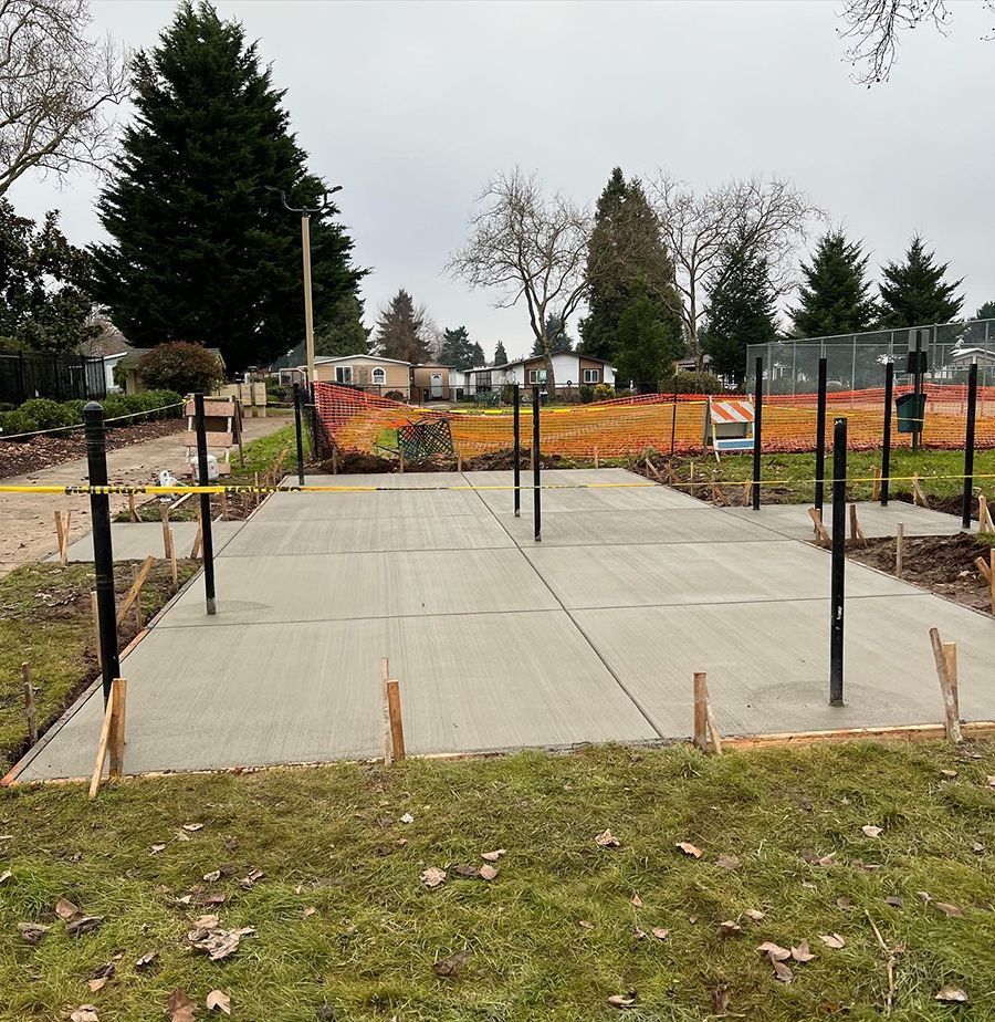 Newly poured concrete slab with metal posts and wooden framing, set in a park.