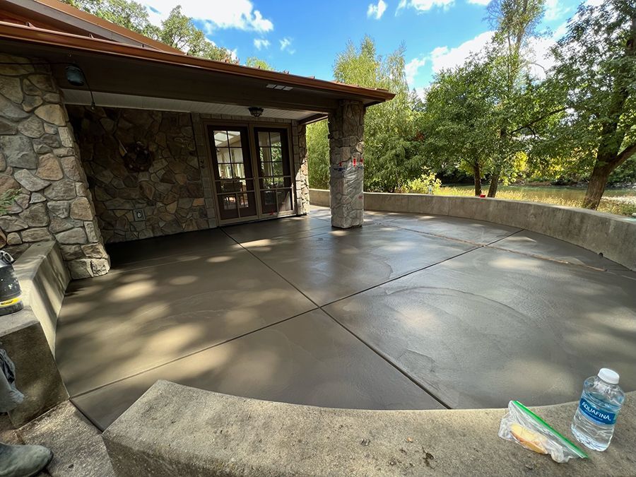 Stone building with a concrete patio. Clear blue sky, green trees in background. Water bottle and bag on patio.