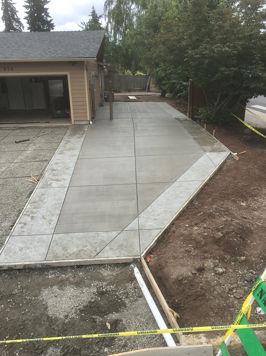 New concrete driveway in front of a tan garage. Diagonal and rectangular panels, yellow caution tape on the right.