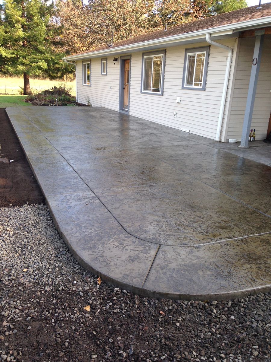 Newly poured concrete patio next to a house with gravel and grass areas.