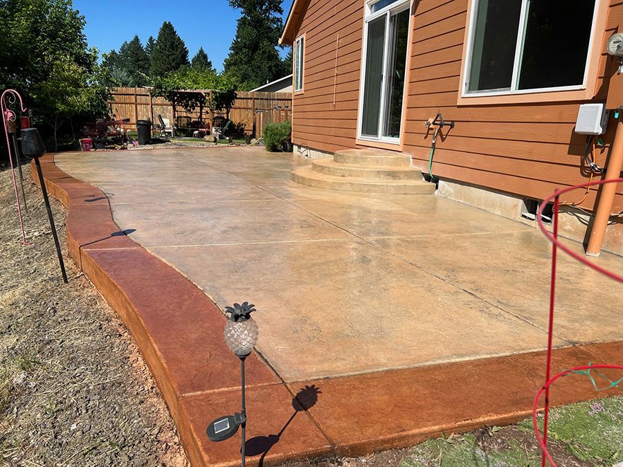Concrete patio with brown stained border next to a house with sliding glass door.