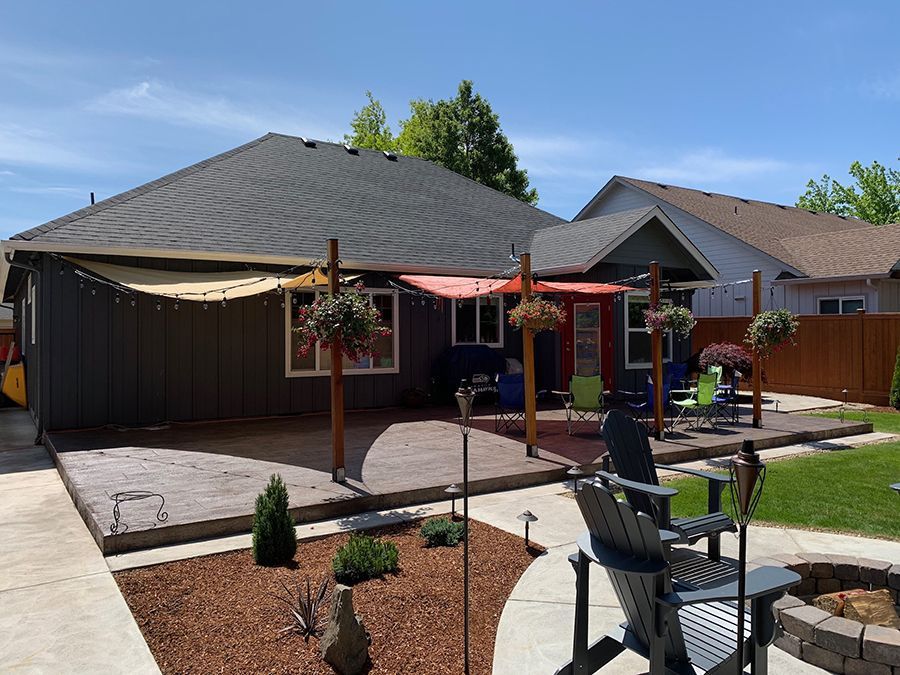 Backyard patio with seating, garden beds, and sun sails on a sunny day.