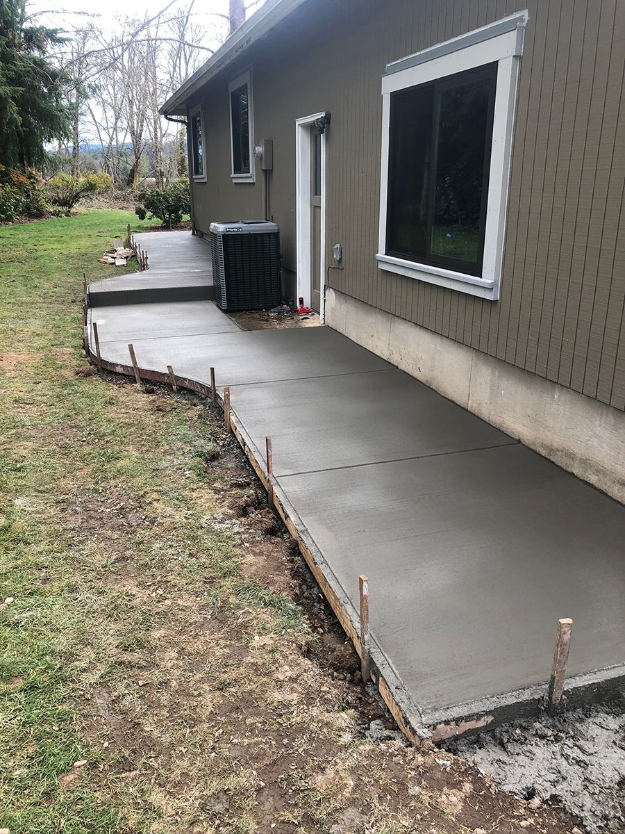 Fresh concrete patio and walkway next to a house with an air conditioner.