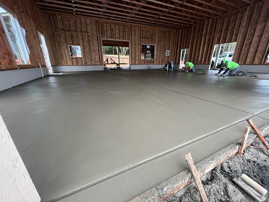 Workers smoothing wet concrete floor inside a wooden-framed building.