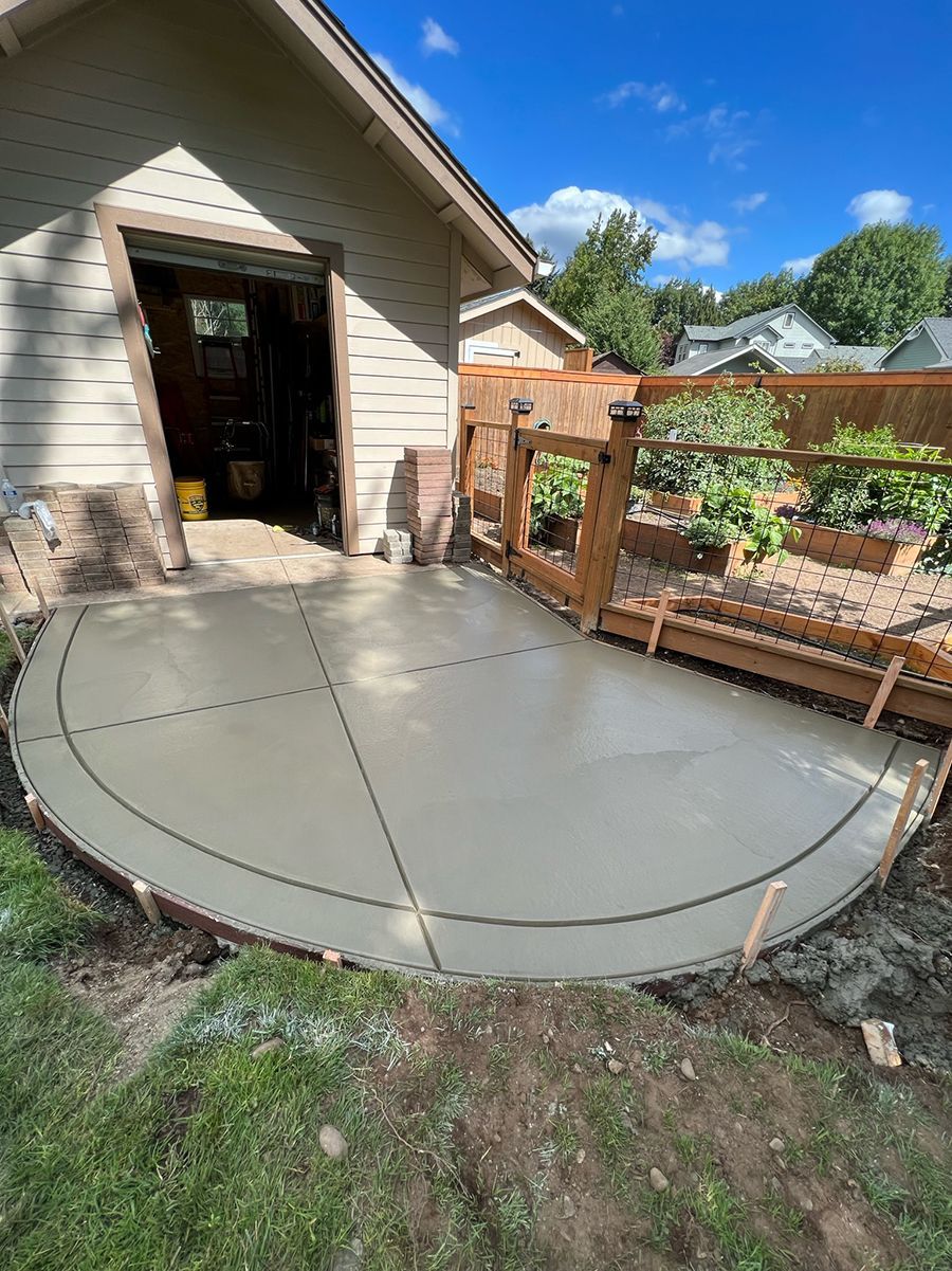 Newly poured concrete patio beside a building and garden.