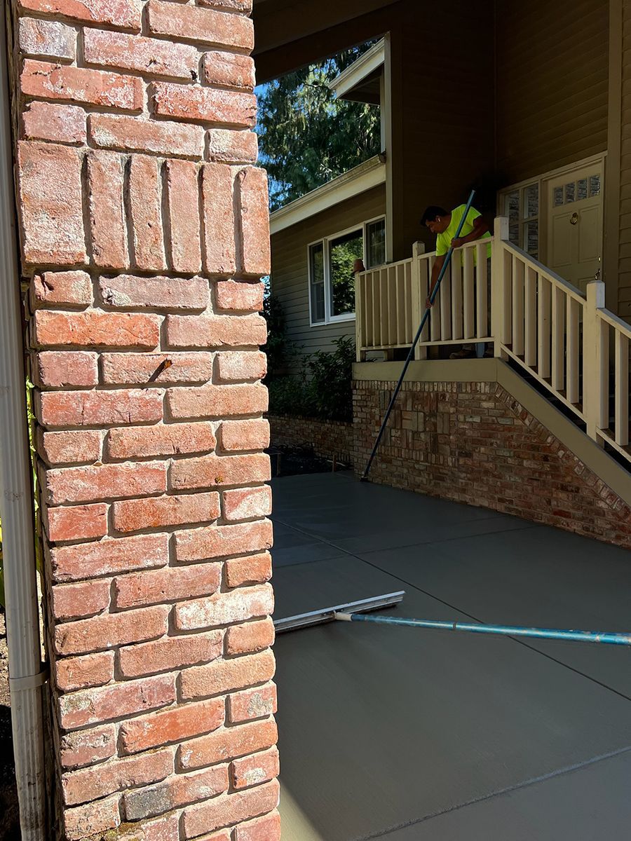 Brick column beside newly poured concrete patio with worker using a leveling tool.
