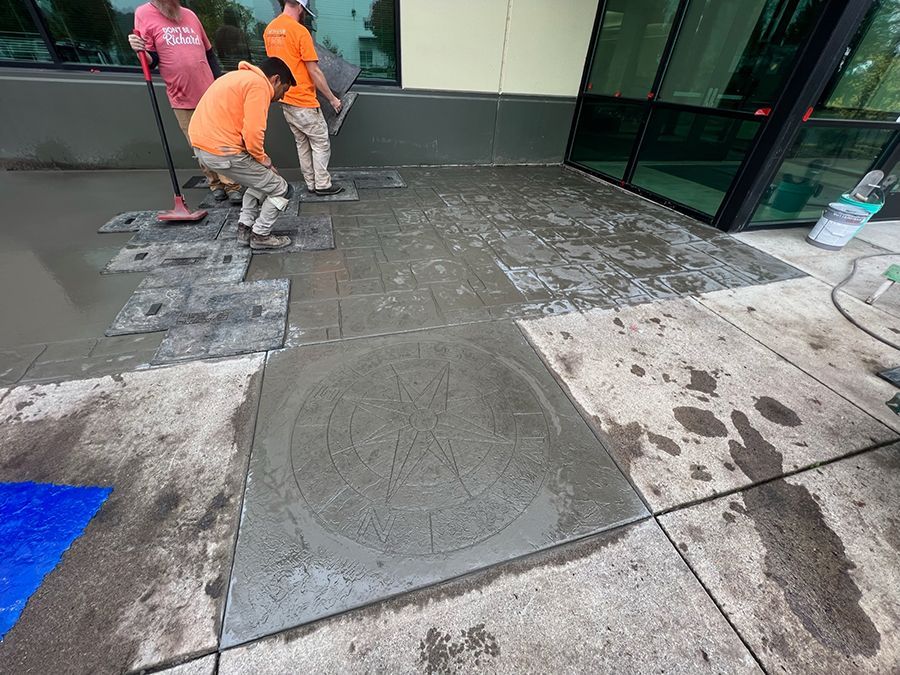 Workers laying concrete tiles outside a building. One worker levels concrete with a trowel.