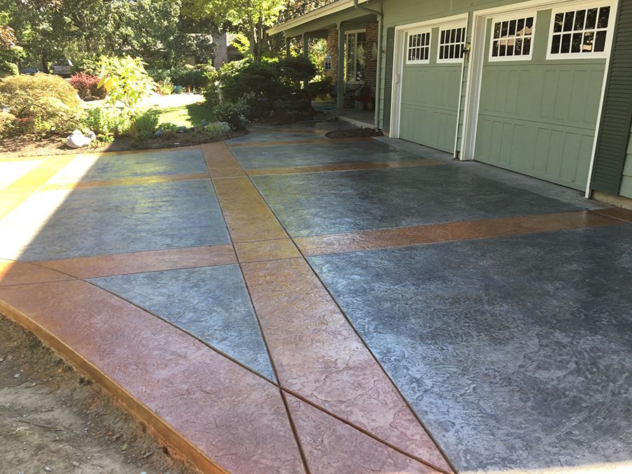 Concrete driveway with geometric brown and gray patterns next to a green garage.
