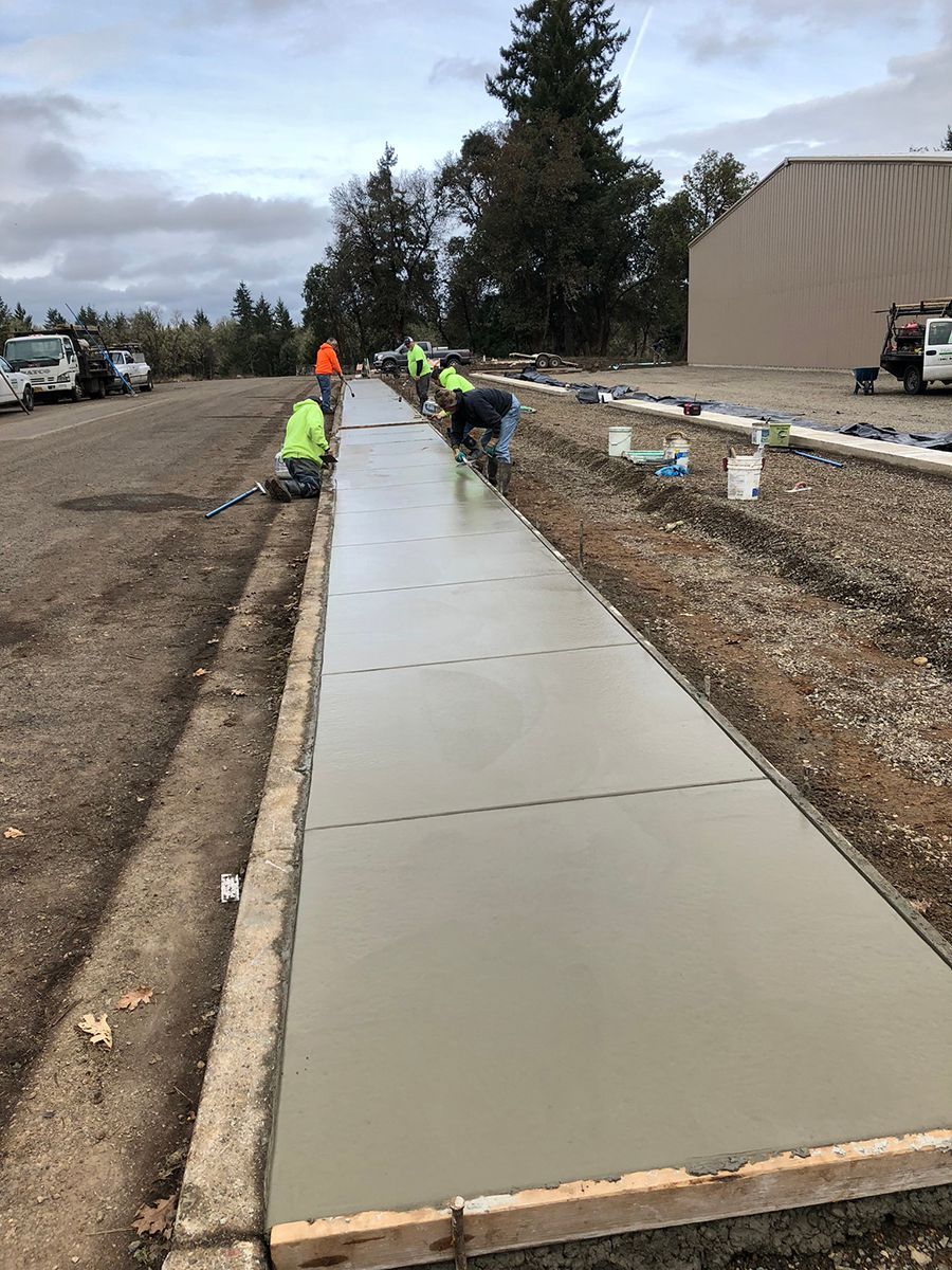 Workers pouring and smoothing fresh concrete for a sidewalk outdoors.