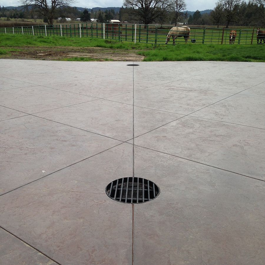 Circular drain in a concrete surface with intersecting lines, green field, and grazing animals in background.