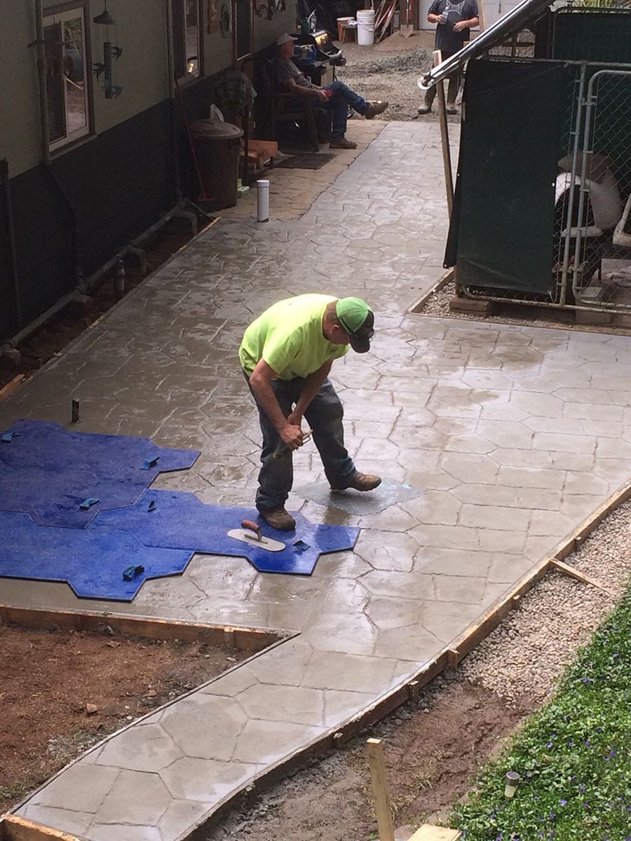Man in green shirt stamps concrete walkway with textured pattern tool.