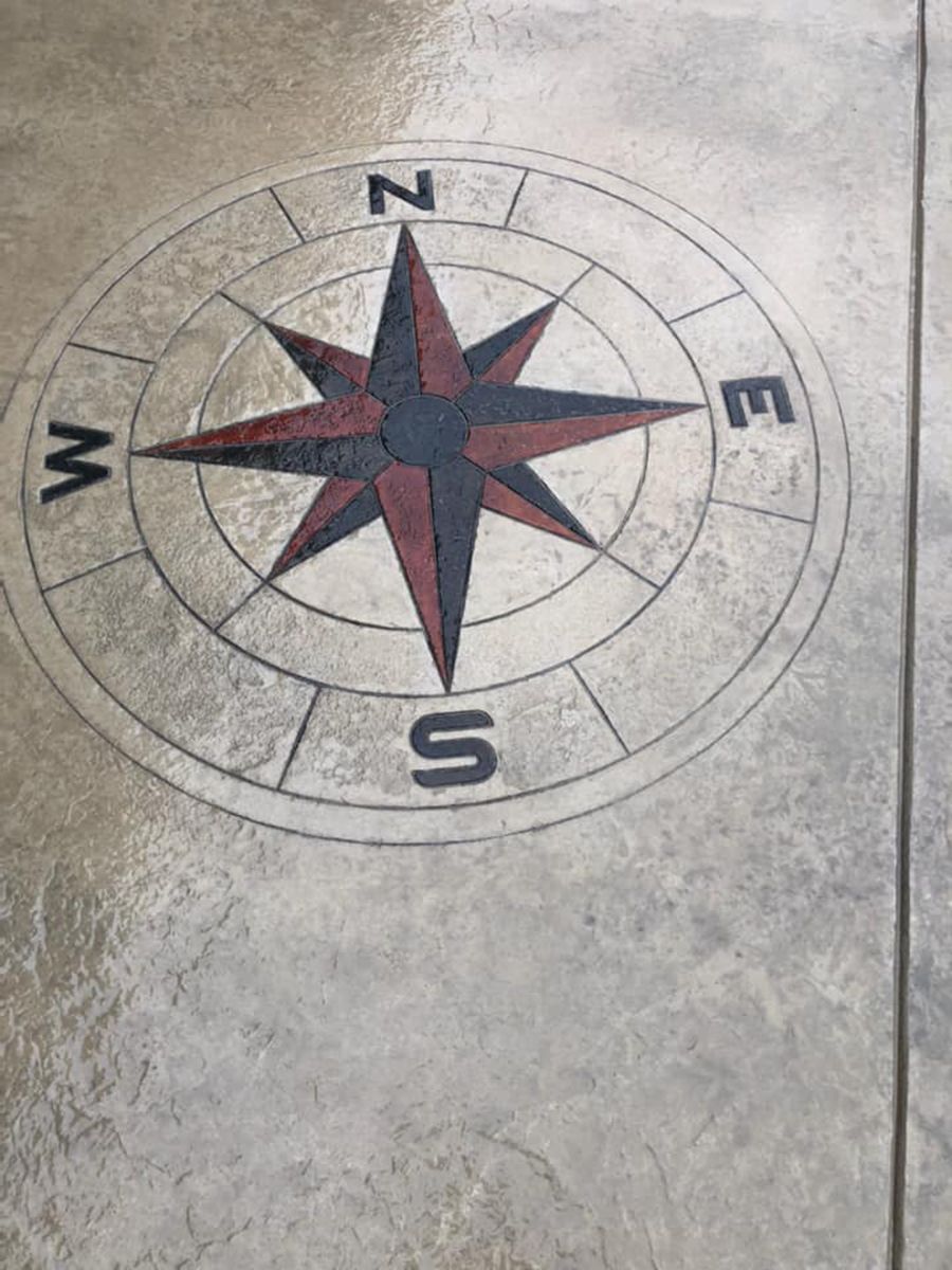 Compass rose design embedded in concrete, with North, East, South, West labels. Red and black accents.