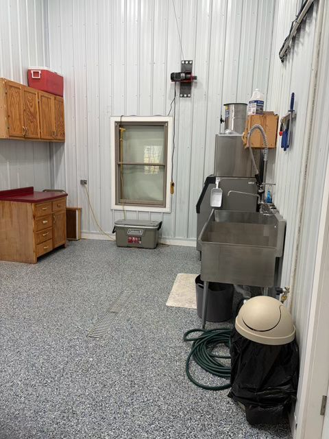 Workshop interior with metal walls, stainless steel sink, cabinets, window, and speckled floor.