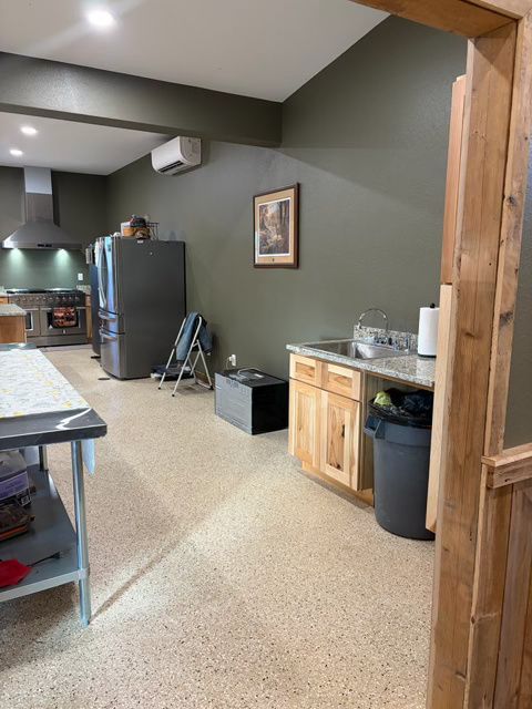 Kitchen interior with a stainless steel stove, refrigerator, cabinets, and a granite countertop. Green walls and a speckled floor.