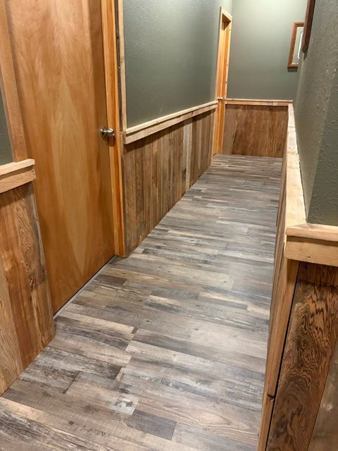 A narrow hallway with wood trim and wood-look flooring. A door is on the left.