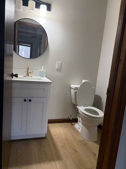 Small bathroom with a white vanity, toilet, and a round mirror.
