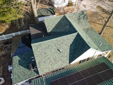 Overhead view of a house with green roof shingles and solar panels, and a white picket fence.