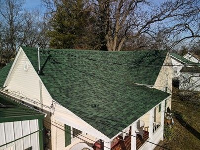 Green shingled roof on a house with white siding and a porch, set in a yard with bare trees.