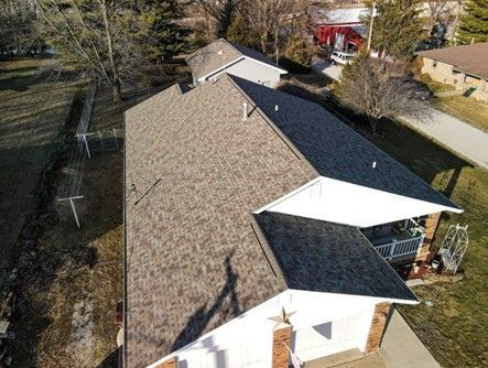 Aerial view of a house with a brown roof. White trim and a porch are visible. A chimney extends from the roof.